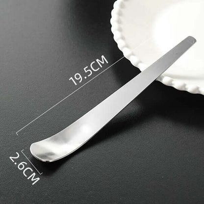 Minimalist dessert spoon 19.5cm x 2.6cm on a black surface, next to a white plate. Ideal for ice cream or coffee.