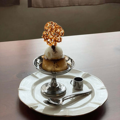 Elegant dessert cup featuring ice cream with a caramel decoration, served on a stainless steel dish with a spoon and mini pitcher.