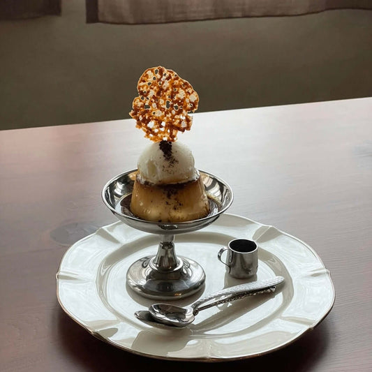 Elegant dessert cup featuring ice cream with a caramel decoration, served on a stainless steel dish with a spoon and mini pitcher.
