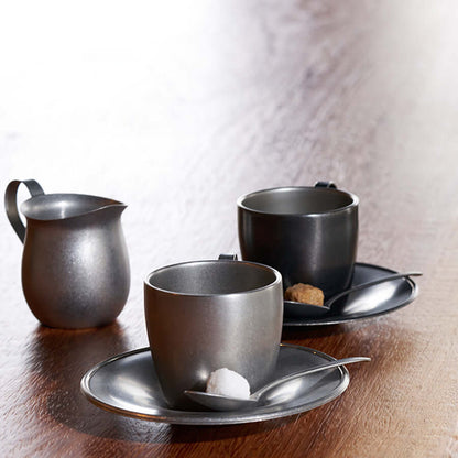 Stainless steel vintage inox cup and saucer with coffee on a windowsill, greenery in background.