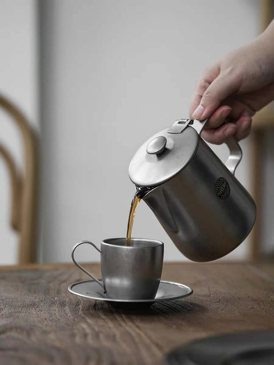 Pouring coffee from VINTAGE INOX stainless steel cafe pot into matching cup, showcasing durable and chic design. Made in Japan.