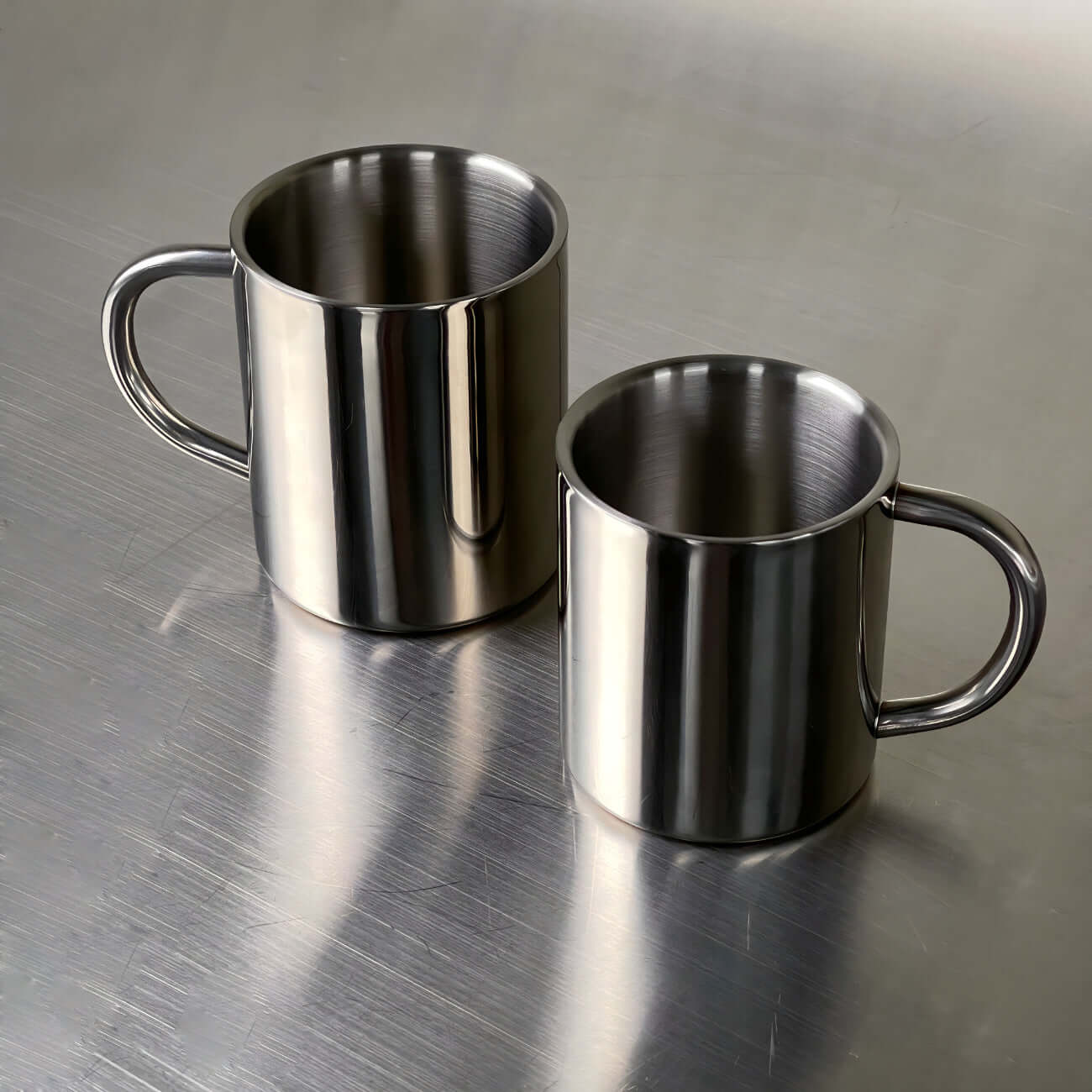 Double-layer glossy stainless steel cups on metallic surface, modern elegance, perfect for temperature control and any occasion.