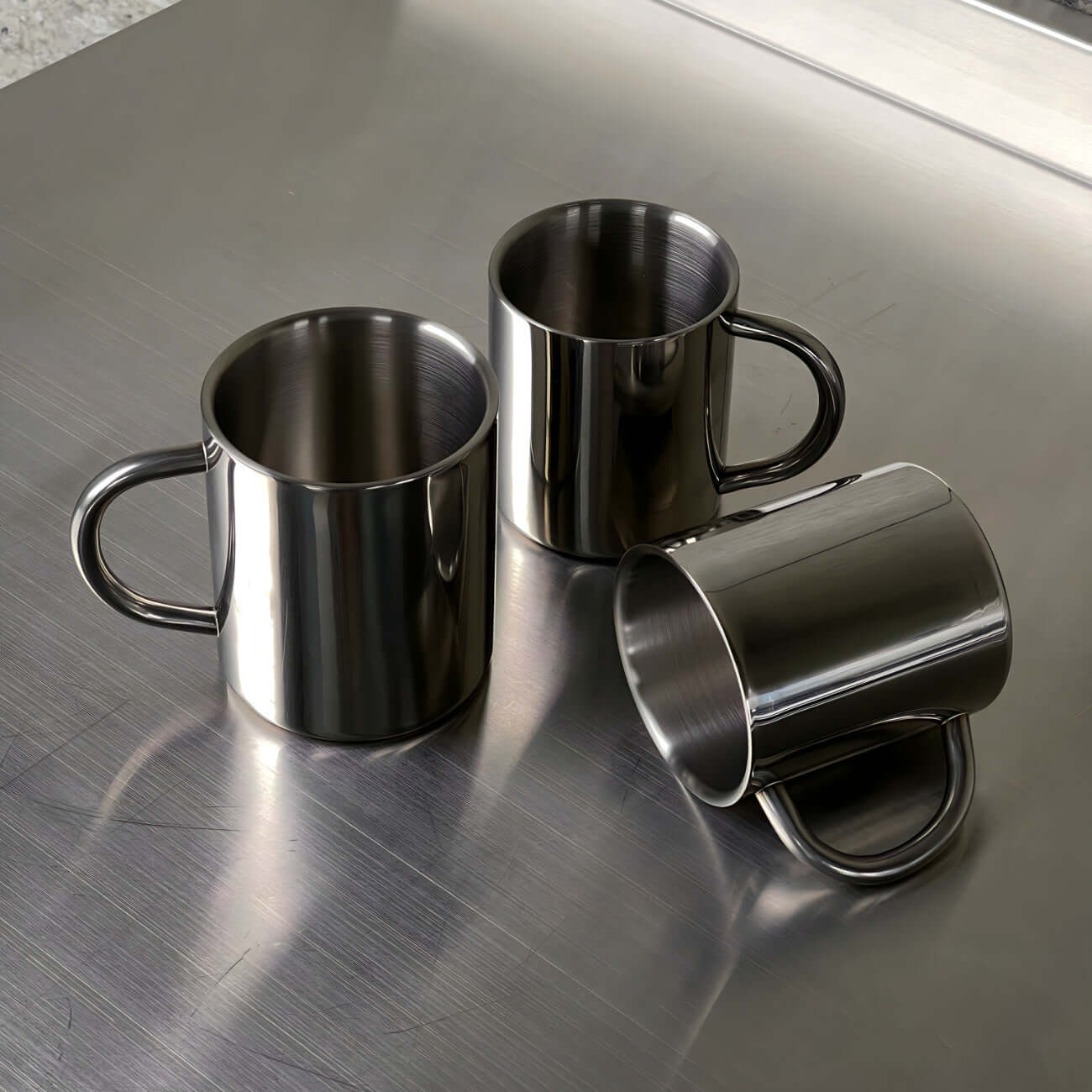 Double-layer glossy stainless steel cups on metallic surface, modern elegance, perfect for temperature control and any occasion.